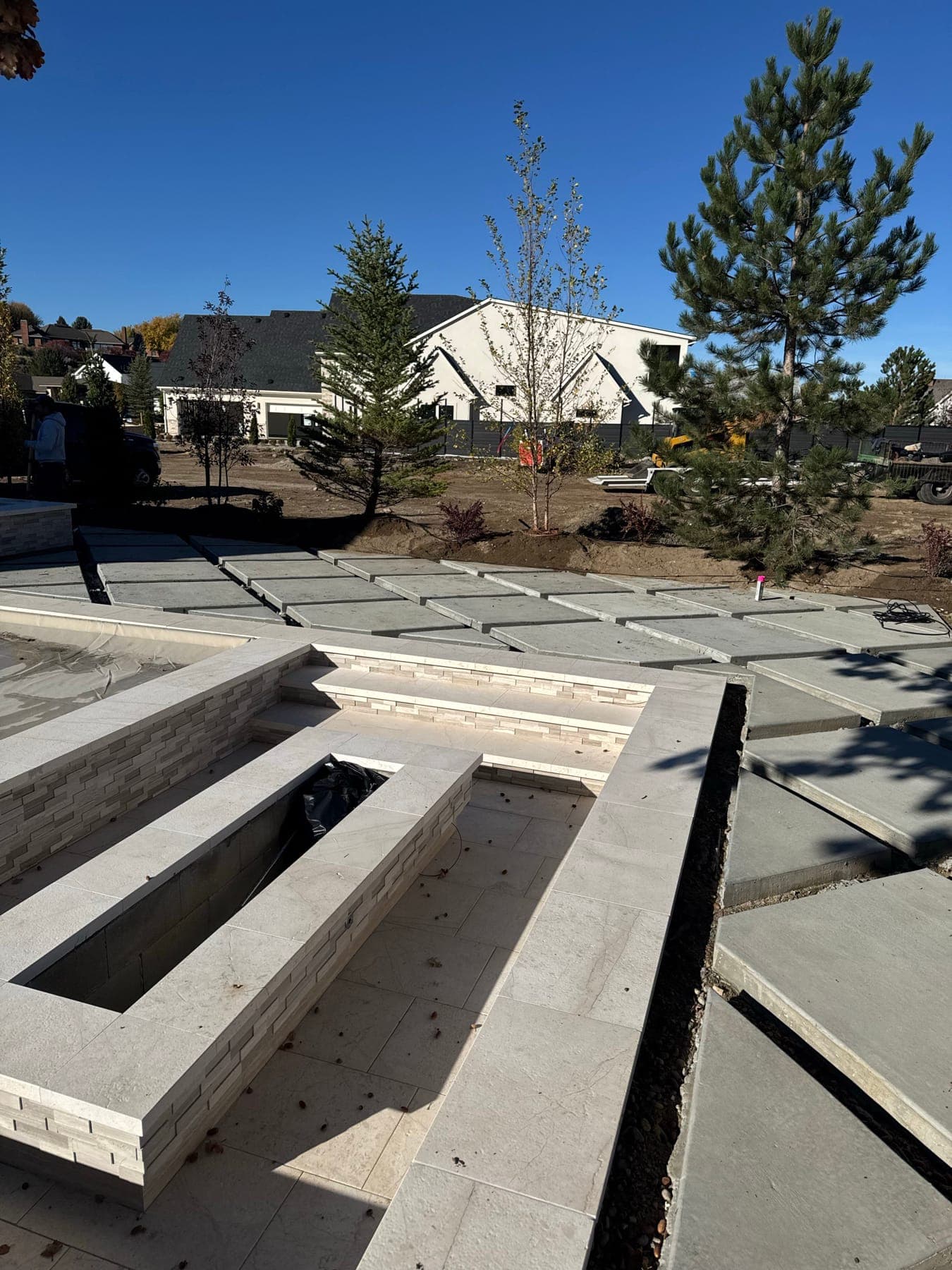 Stone-clad fire feature and large-format concrete pavers mid-installation